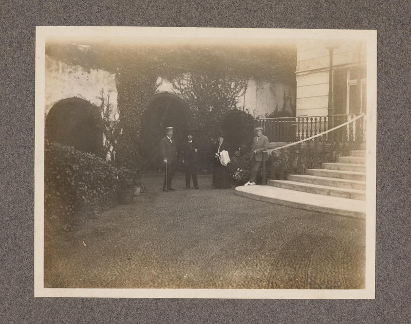 No caption [white men and a woman in front of building]