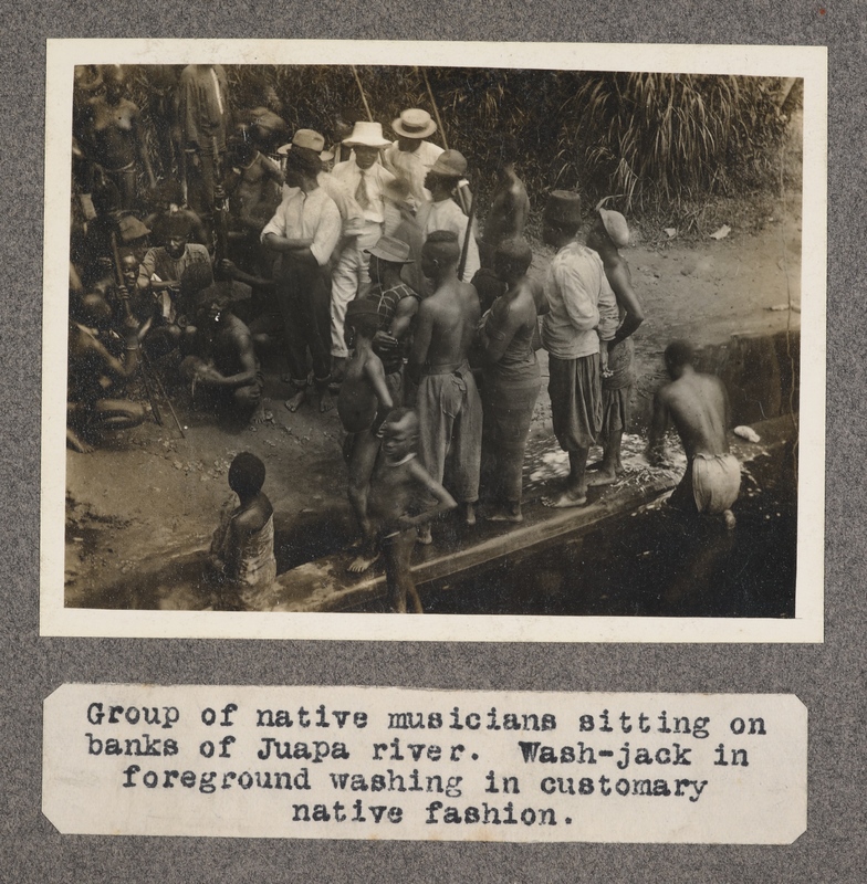 Group of native musicians sitting on banks of Juapa River. Wash Jack in foreground washing in customary native fashion